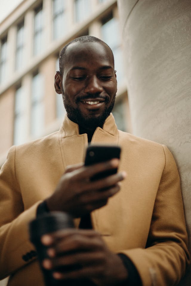 رجل يبتسم وهو ينظر إلى هاتفه الذكي.
