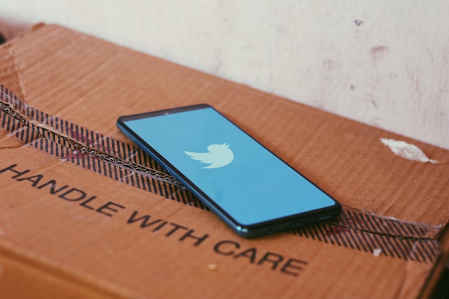 Un teléfono negro sobre una caja de cartón con la pantalla azul de Twitter abierta.