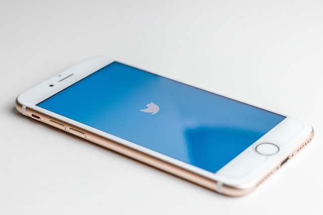 Un iPhone 6S dorado colocado sobre fondo blanco con la pantalla azul de Twitter abierta