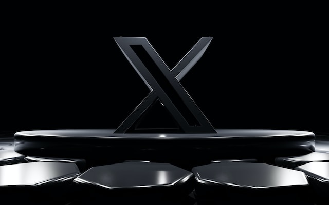 Imagen de un logotipo X negro sobre una plataforma circular en un fondo negro.