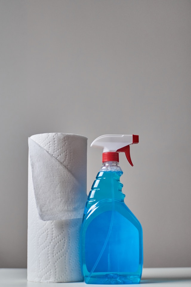 Un rollo de toalla de papel junto a una botella de spray con un líquido azul.
