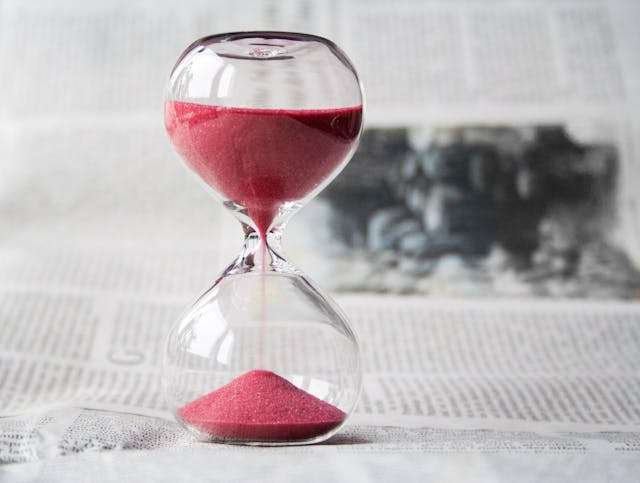 Un reloj de arena transparente con arena roja sobre un periódico.