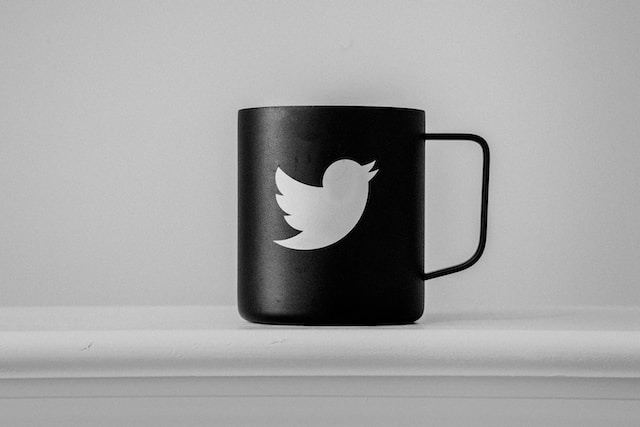 Ilustrasi cangkir hitam dengan cetakan logo Twitter dengan latar belakang putih.
