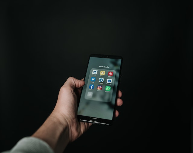 Gambar seseorang yang memegang ponsel hitam yang menampilkan folder aplikasi media sosial yang berisi Twitter dan aplikasi lainnya