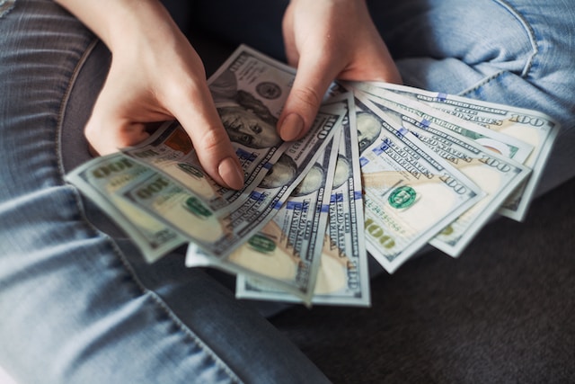 Gambar close-up seorang wanita yang duduk di atas karpet dengan uang kertas dolar yang terhampar di tangannya.