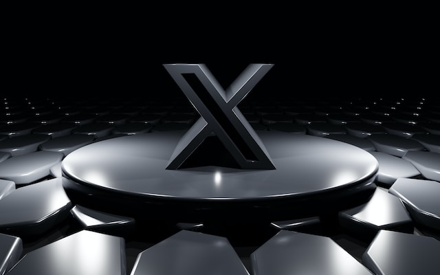 Ilustrasi logo X hitam pada platform melingkar yang dikelilingi oleh latar belakang hitam.