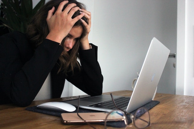 Gambar seorang wanita yang memegangi kepalanya dengan frustrasi sambil melihat layar Macbook.