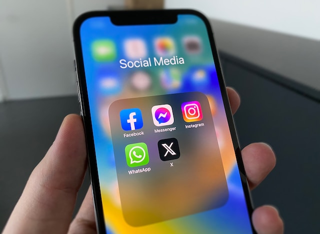 Gambar tangan yang memegang ponsel hitam yang menampilkan aplikasi Twitter, aplikasi Now X dan aplikasi media sosial lainnya dalam sebuah folder.