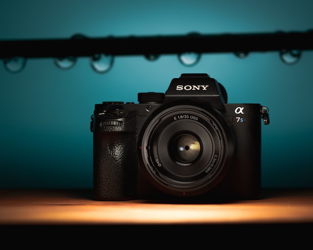 Gambar closeup kamera Sony hitam yang diletakkan di atas meja kayu. 