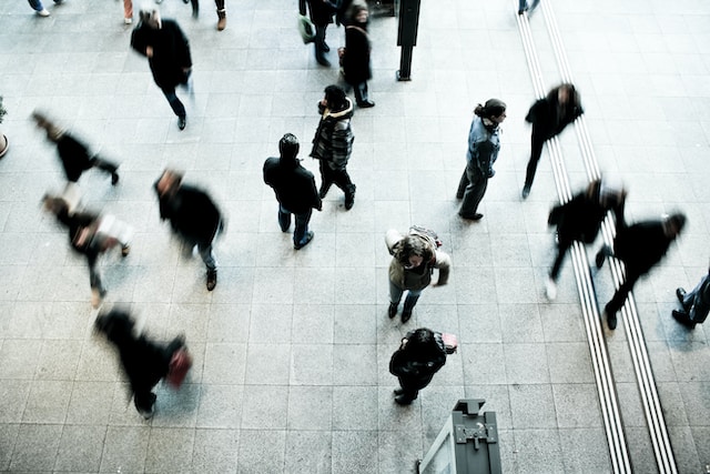 Un'immagine di una stazione degli autobus che evidenzia un uomo al centro con persone sfocate che passano tutt'intorno.
