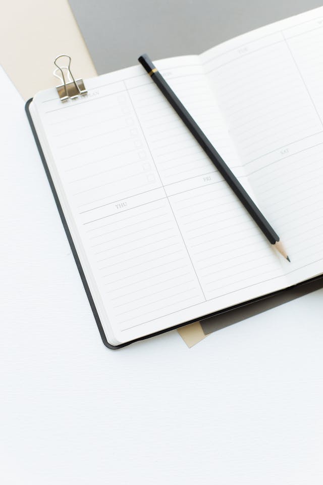Una pagina vuota di un'agenda con una matita nera e un fermaglio di metallo grigio.
