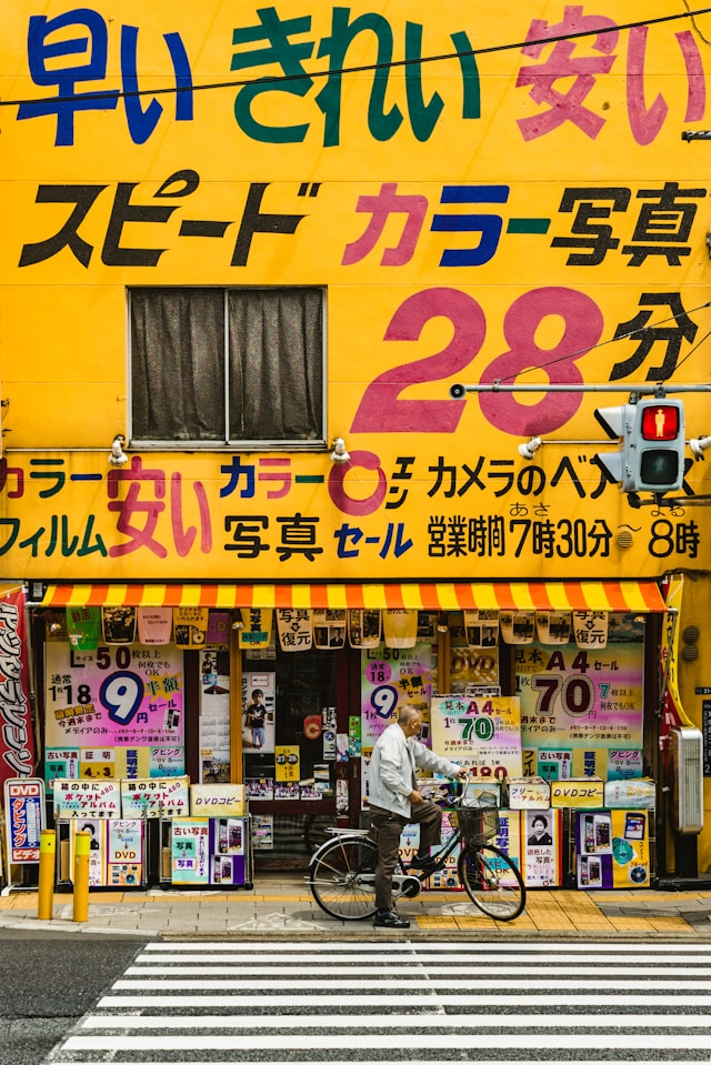 日本語の書かれた黄色い店の前で自転車に乗った男。