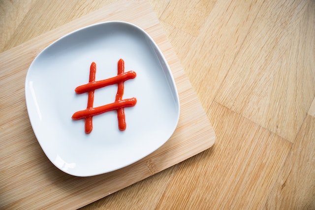 Een foto van het hashtagteken geschreven met ketchup op een wit bord van keramiek