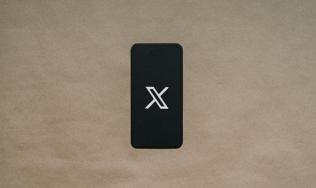 Een afbeelding van het X-logo op een zwarte smartphone op bruin papier.
