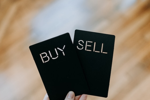 Uma imagem de uma mão que segura dois cartões pretos com "BUY" e "SELL" escritos. 