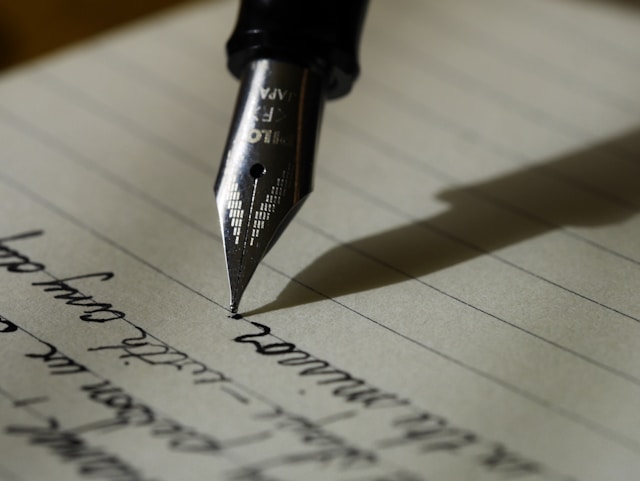 Um close da ponta de uma caneta de tinta ao lado de uma folha de papel com linhas horizontais.

