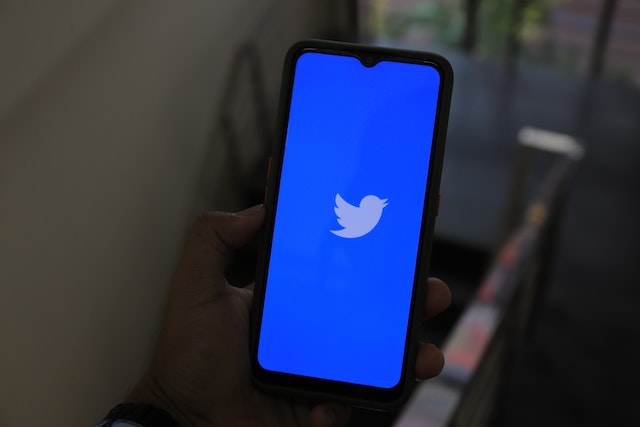 A photograph of someone holding a smartphone with Twitter’s blue welcome screen displayed on the screen. 
