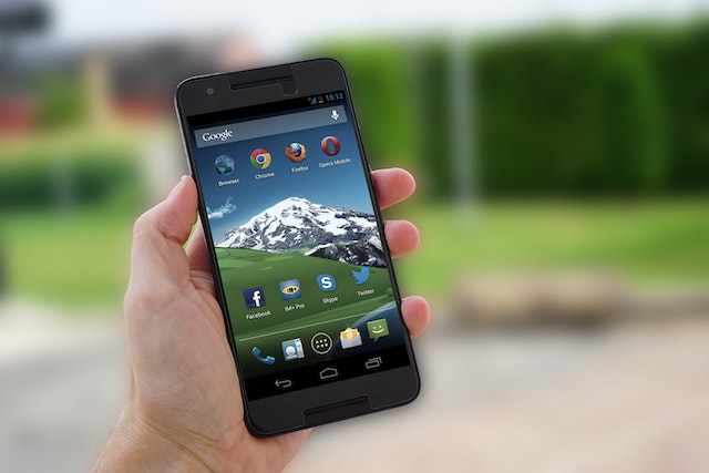 A picture of someone holding a black Android phone with several apps, including Twitter, on its home screen.
