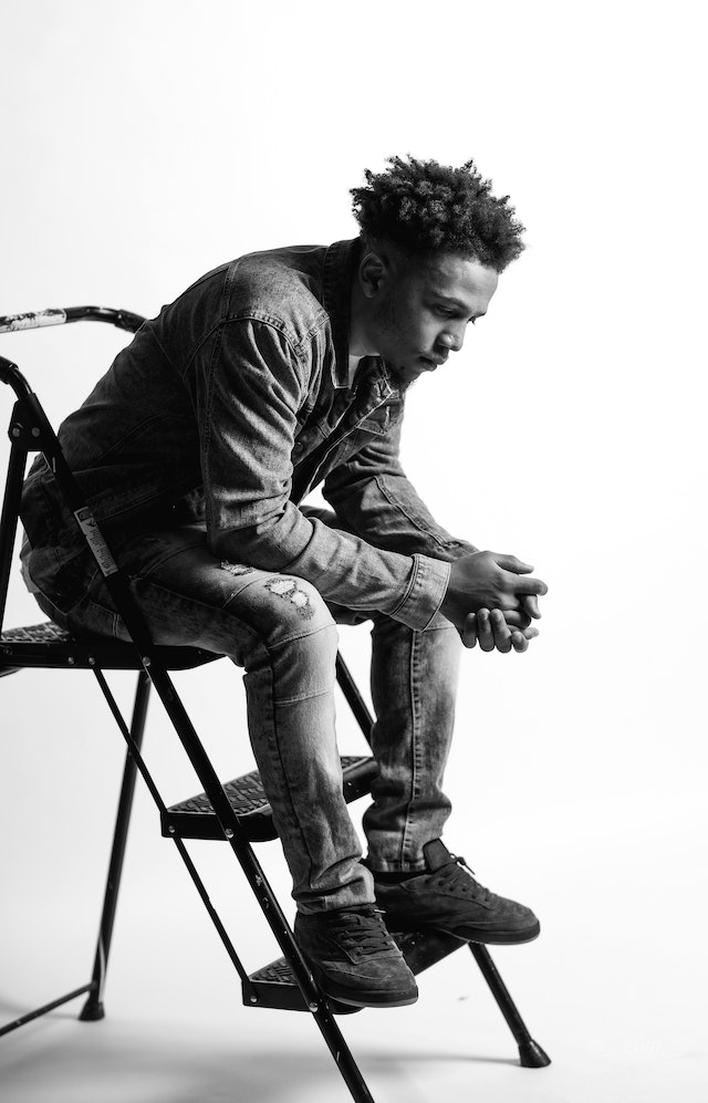 A monochrome photo of a man thinking while he sits on a step ladder.