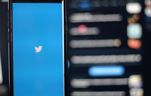 A photo of a mobile phone in a blurry background displaying the Twitter logo on the screen.
