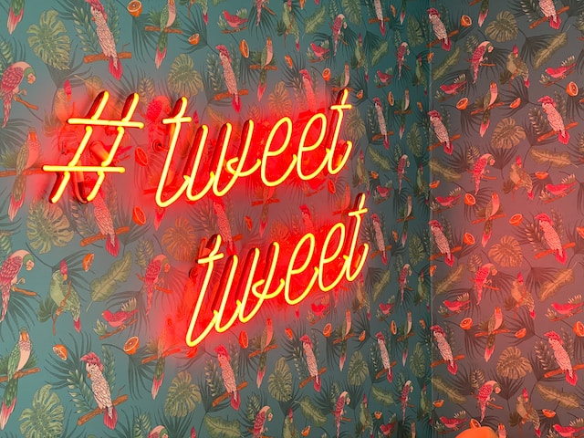 A neon sign on a wall that says “# tweet tweet.” 
