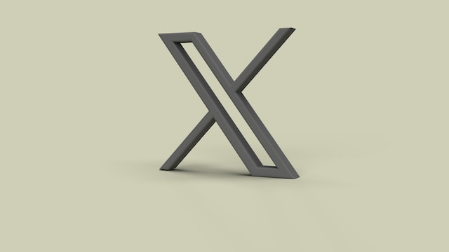A 3D image of Twitter’s new X logo depicted in gray on a light umber-colored background.