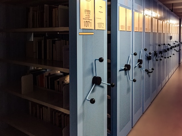 A photo of a library archive with distinct shelves bearing detailed labels.