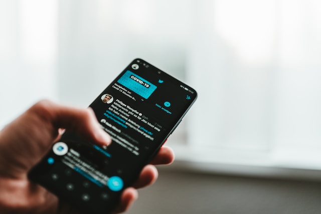 A photograph of a person holding a phone displaying a Twitter feed.