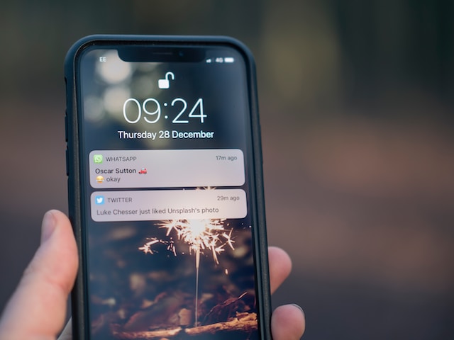 A picture of a person holding a phone with the lock screen showing push notifications from WhatsApp and Twitter.