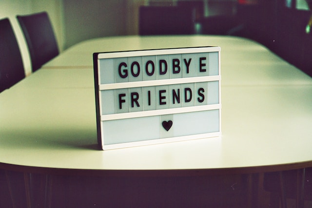 A photograph of a mini signpost placed on a table with the inscription “GOODBYE FRIENDS” and a heart symbol below.