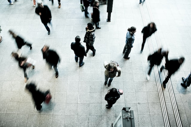 A picture of a bus station highlighting a man in the middle with blurry people passing all around.