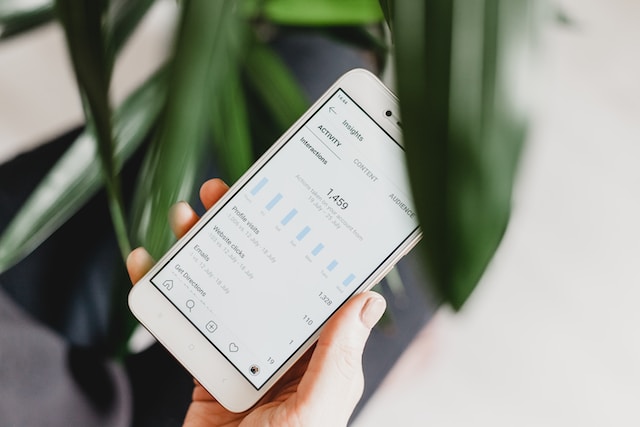 A photo of a hand holding a phone displaying the analytics of a social media account.