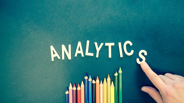 A picture of a hand arranging letters on a board to spell the word “ANALYTICS.”
