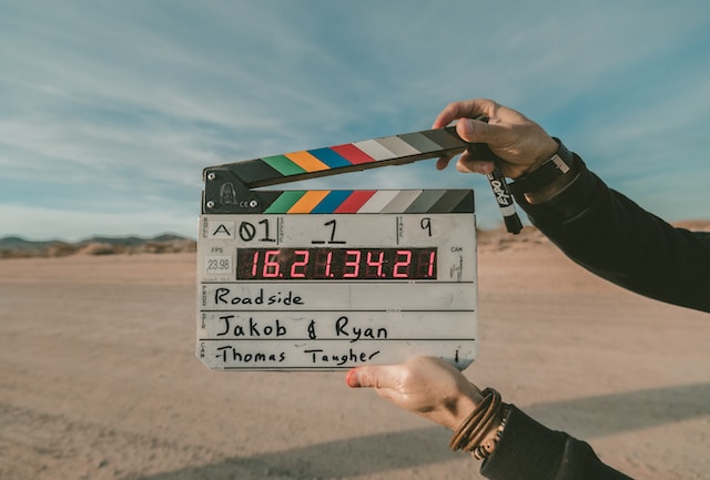 Uma fotografia de mãos a segurar uma claquete durante uma filmagem de vídeo.