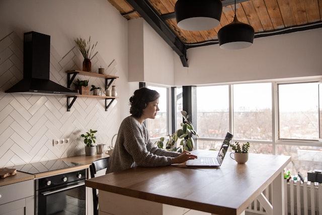 Mujer sentada en una cocina con auriculares mientras cambia la configuración de su cuenta de Twitter en el ordenador.