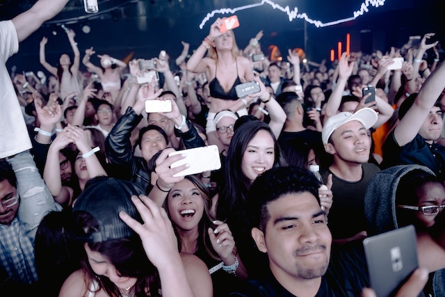A picture of an audience mostly using their phones to take photos of a performer.