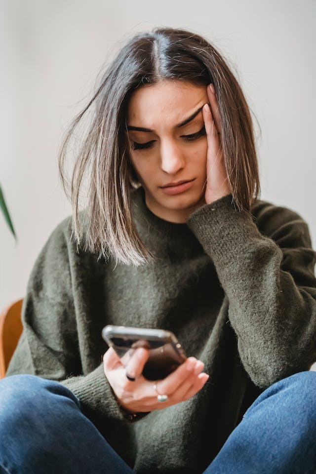 A concerned woman looking at her smartphone, trying to find her old Twitter username and log-in information for X.