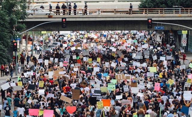 A large group of protestors holding signs while the police watch them from a bridge.