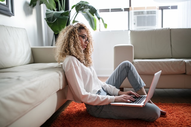 A woman sitting on her floor and typing on her laptop.