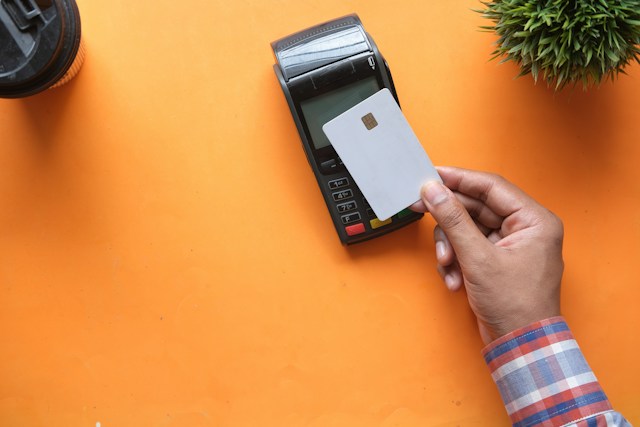 A person taps their card on a magnetic card reader on an orange table.