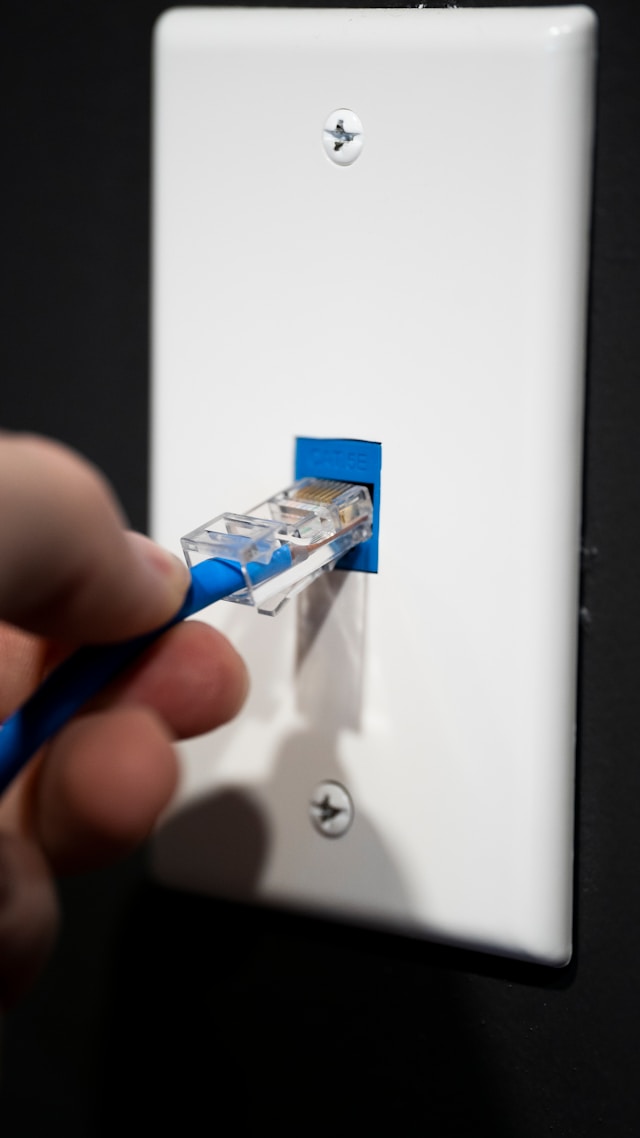 A person unplugs an RJ45 connector with a blue cable from a wall socket.