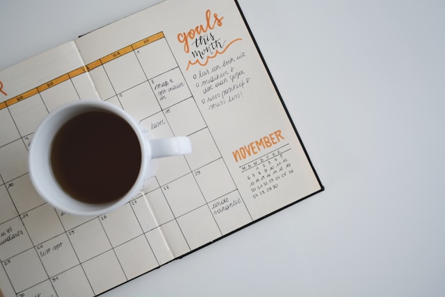 A white cup with a brown liquid on a calendar book.