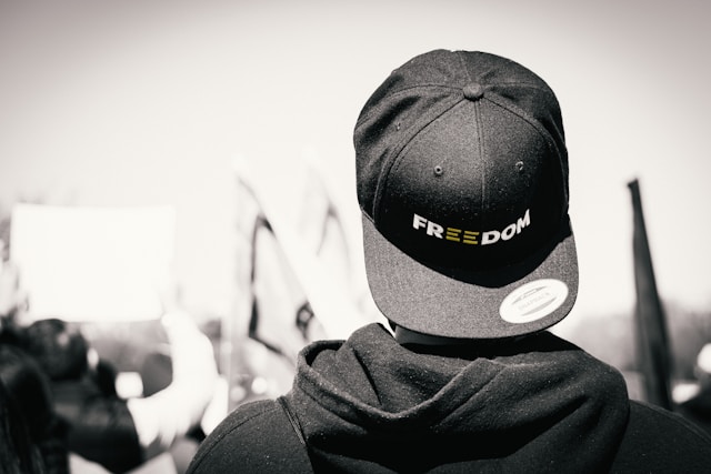 A person with a hoodie wears a snapback cap backward with the word freedom.