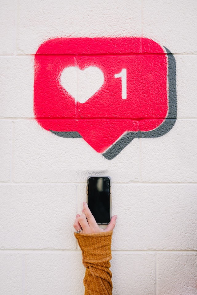 A person holds an iPhone under a red chat bubble and a heart and number one in white.