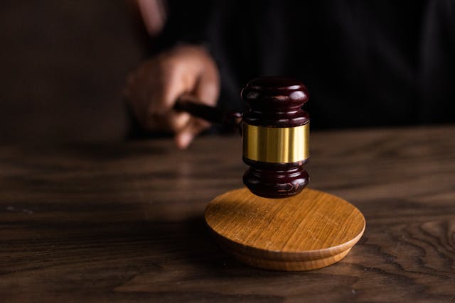 A person holds a dark maroon gavel with a golden strip above a circular sound block.