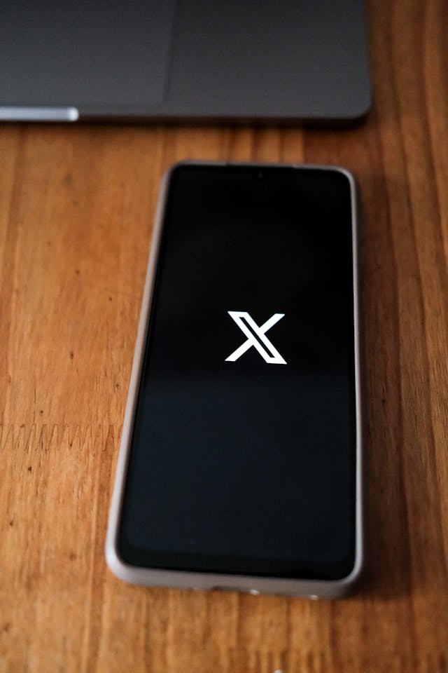 A smartphone with the Twitter app’s splash screen on a wooden table.
