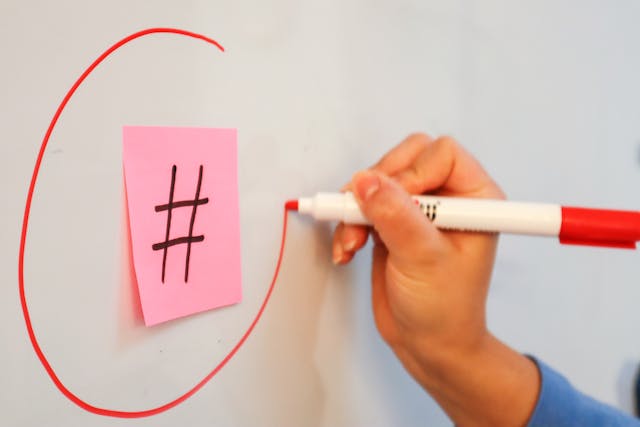 A person uses a marker to draw a red circle around a pink note with the hash symbol.