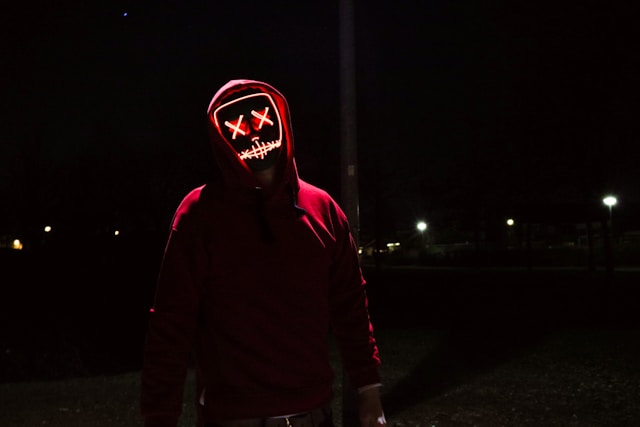 A person with an LED mask and a red hoodie at night.