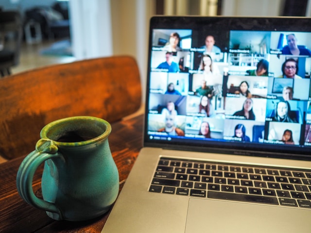 A video group chat with multiple participants on a gray Macbook Pro next to a green cup.
