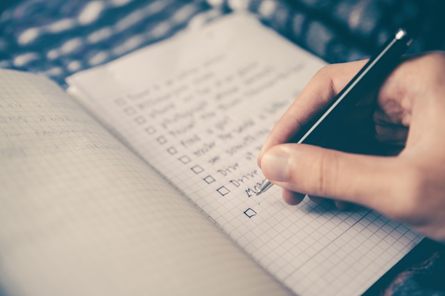 A person writes a checklist in a notebook with a black pen.
